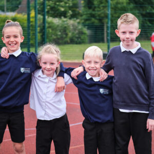 SBPA4 Four boys in varying heights and ages, stood with arms across one anothers' shoulders, smiling.