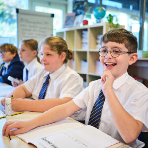 TPA4 White boy, approximately aged 10, with circular glasses looking into the distance whilst smiling sat at a desk